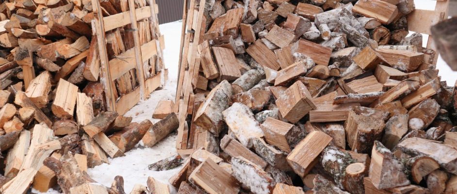 Wooden box with firewood. Chopped and hand-folded in a crate for sale or for storage in a cottage. transport by pallet truck. Large pile of Firewood outside in the snow